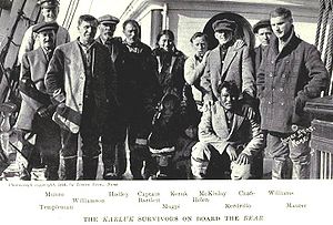  Ten men, one woman and two children stand (one man crouching) on a ship's deck. Both children are largely obscured in shadow. The men's clothes look haphazard, and the facial expressions of most are sombre and weary, although a few are attempting to smile.