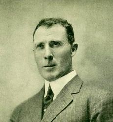Head and shoulders photograph of man facing half-left. Age about 35, short dark hair, light-coloured jacket, white shirt with high collar.
