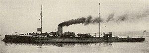 A long, slender ship with a tall smoke stack belching thick black smoke.
