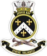 A ship's badge. A naval crown sits on top of a black scroll with "JERVIS BAY" written in gold. This is atop a yellow, rope-patterned ring, which contains a black field. Three gold fleur de lys are positioned at the bottom, upper left, and upper right: the bottom one is deparated from the other two by a white chevron containing eight black marks. Below the ring are a stone axe and a nulla nulla sitting on top of a boomerang. At the bottom of the badge is a black scroll with "STRIVE VALIANTLY" written.