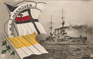 A large white life-preserver with the words "S.M.S. Hannover," the black and white flag of the German Navy, and a white and yellow flag are superimposed on a photo of a large gray warship; thick black smoke drifts from its three smoke stacks
