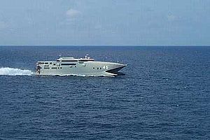 A warship-grey catamaran travelling at speed (from right to left) on the open sea